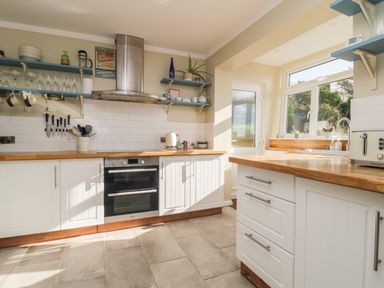A kitchen with white cabinets wooden countertops shelves with dishes and knife set at Ocean View in Downderry