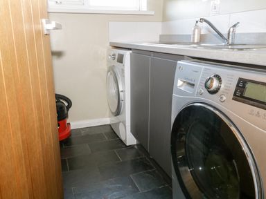 A laundry room with a washing machine dryer sink vacuum cleaner and tiled floor at Ocean View in Downderry
