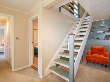 A staircase with green and white steps next to a corner with built-in shelves and an orange armchair at Ocean View in Downderry