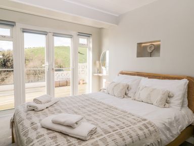 A bedroom with a bed and pillows near large glass doors overlooking a patio at Ocean View in Downderry