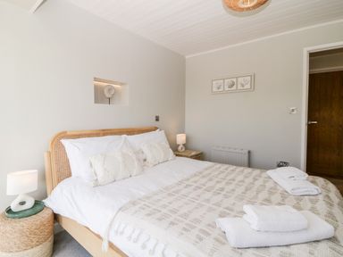 A bedroom with a wooden bed frame white bedding patterned blanket bedside tables with lamps and towels on the bed at Ocean View in Downderry
