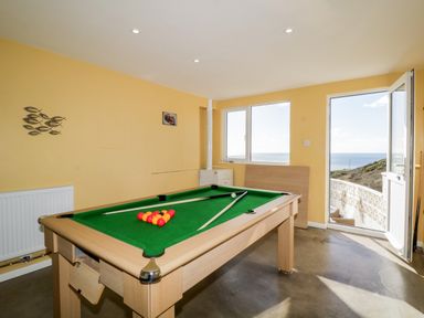 A game room with a pool table next to a window and an open door showing a sea view at Ocean View in Downderry