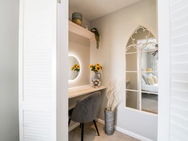A small vanity area with a chair a round illuminated mirror a vase with sunflowers and a tall decorative vase with dried branches at Ocean View in Downderry