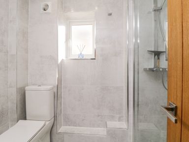 A bathroom with a toilet a small window and a glass-enclosed shower at Ocean View Downderry
