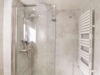 A bathroom shower area with glass door and a white wall-mounted radiator at Ocean View in Downderry