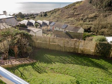 A garden with a wooden trellis fence overlooking houses and a hillside with the sea in the background at Ocean View in Downderry
