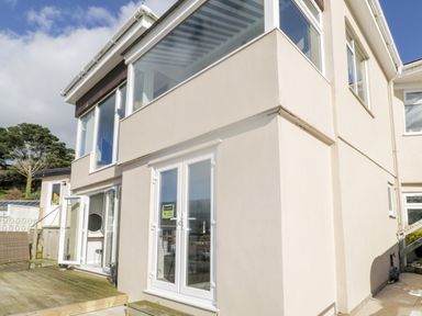 Outside view of a two story building with multiple windows and glass doors leading to a wooden deck at Ocean View in Downderry