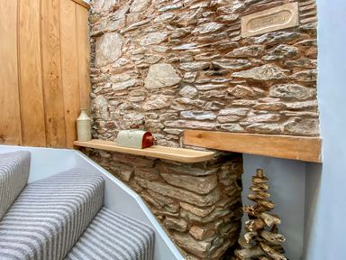 A stone wall beside carpeted stairs with a wooden shelf holding a jug and a small box at Pilchard Cottage in Brixham