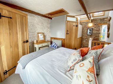 A bedroom with a bed with patterned pillows a wooden door a dressing table with a mirror and a stone wall at Pilchard Cottage in Brixham