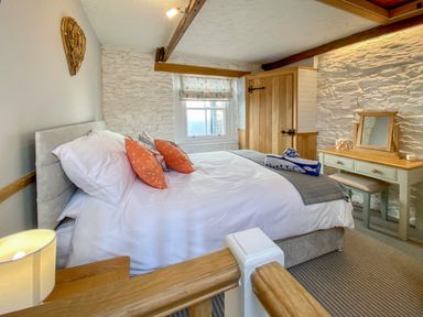 A bedroom with a bed with orange pillows a wooden wardrobe and dressing table at Pilchard Cottage in Brixham