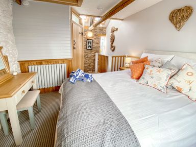 A bedroom with a bed with patterned pillows a wooden dressing table and a door with stone walls at Pilchard Cottage in Brixham