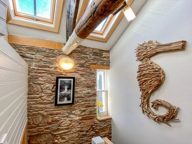 A stairwell with framed lighthouse picture on a stone wall and seahorse wall art made of wood at Pilchard Cottage in Brixham