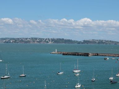 Sea with boats and a pier with a lighthouse and a view of land with houses across the water at Pilchard Cottage in Brixham