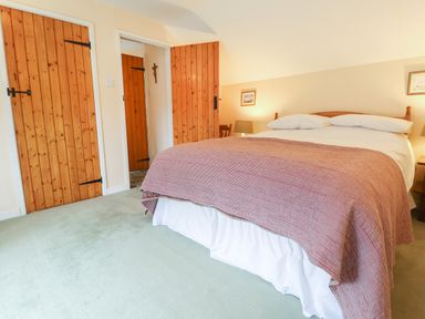 A bedroom with a bed covered by a red blanket and wooden doors at Penllain in Newport Pembrokeshire