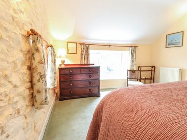 A bedroom with a wooden dresser lamp chair and framed picture at Penllain in Newport Pembrokeshire