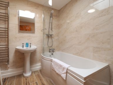 A bathroom with a bathtub shower combo a pedestal sink with soap and a mirror at Penllain in Newport Pembrokeshire