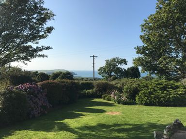 A garden with grass, bushes, trees, and a view of the sea at Penllain Newport Pembrokeshire