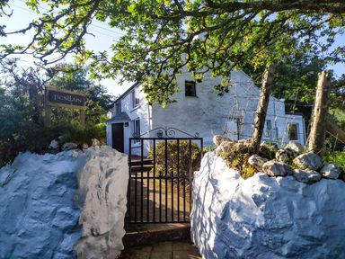 A white stone house behind a black metal gate and stone wall with a sign reading Penllain in Newport Pembrokeshire