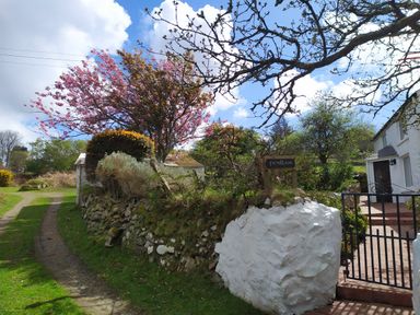 A stone wall with greenery and a wooden sign reading penllain near a white building and a pathway at Penllain in Newport Pembrokeshire