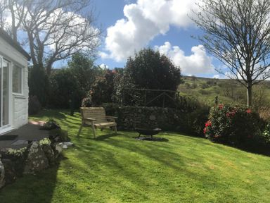 A garden with a wooden bench fire pit trees and shrubs near a white house at Penllain in Newport Pembrokeshire