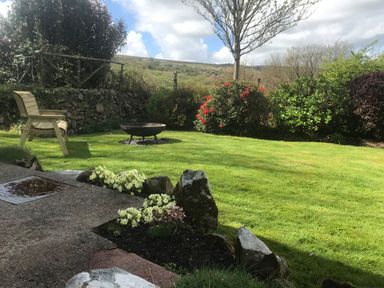 A garden with a fire pit wooden bench stone wall and flowering bushes at Penllain Newport Pembrokeshire