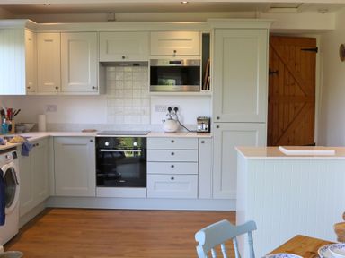 A kitchen with white cabinets wooden floor a microwave kettle toaster and a wooden door at Penllain in Newport Pembrokeshire
