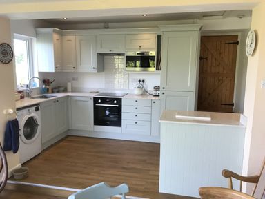A kitchen with white cabinets appliances wooden floor and a wooden door at Penllain in Newport Pembrokeshire