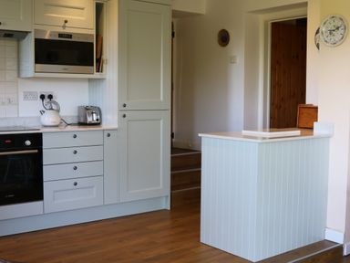 A kitchen with white cabinets a built-in microwave a kettle a toaster and a small island at Penllain in Newport Pembrokeshire