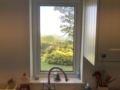 A kitchen sink with a window overlooking green shrubs and a distant hill at Penllain in Newport Pembrokeshire