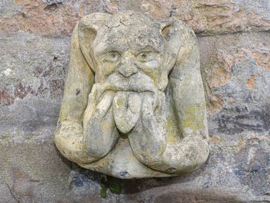 A stone gargoyle sculpture with hands on cheeks and tongue sticking out on a stone wall at Rydal Cottage in Scarborough