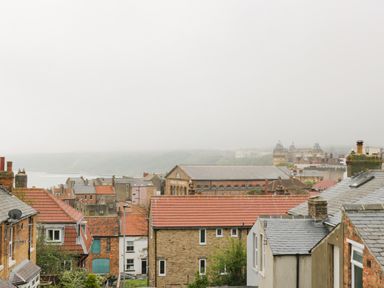 Rooftops of houses with a public market building and hazy view of a distant town and water at Rydal Cottage in Scarborough