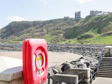 A red life saving equipment box near rocky shoreline with road and hills in background at Rydal Cottage in Scarborough
