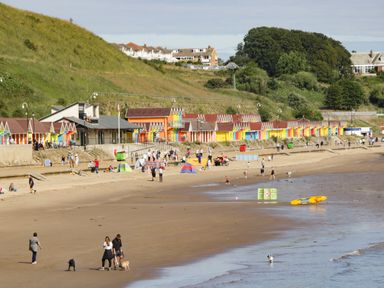 A beach with people walking and colorful beach huts at Rydal Cottage in Scarborough