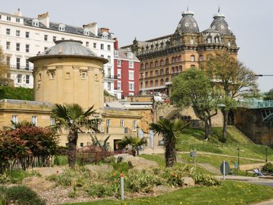 A garden with palm trees and flowers in front of historic buildings in Scarborough