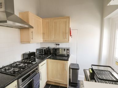 A kitchen with wooden cabinets a gas stove an oven a bread box a toaster a kettle a microwave a trash bin and a dish rack at Rydal Cottage in Scarborough