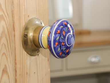 A wooden door with a decorated blue and orange ceramic door knob and a blurred cabinet in the background at Rydal Cottage Scarborough