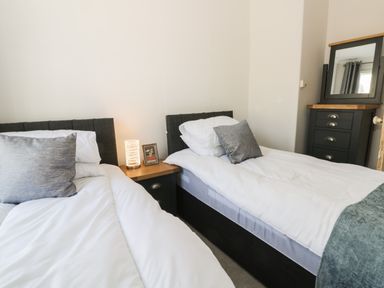 A bedroom with two single beds a nightstand with a lamp and a framed picture and a chest of drawers with a mirror at Rydal Cottage in Scarborough