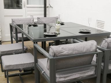 A dining table with glass top and grey cushioned chairs with plates and glasses on the table at Rydal Cottage Scarborough