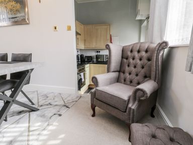 A gray armchair and ottoman next to a kitchen area with wooden cabinets and black countertop at Rydal Cottage in Scarborough