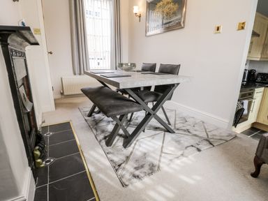 A dining area with a rectangular table, two chairs, and a bench on a rug next to a fireplace at Rydal Cottage in Scarborough