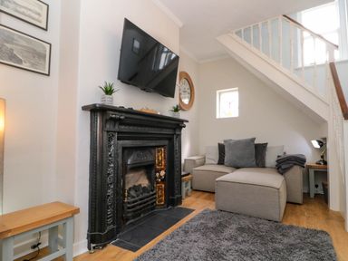 A living room with a grey sofa a black fireplace and a wall-mounted TV at Rydal Cottage in Scarborough