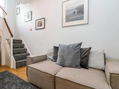 A beige sofa with gray and black cushions next to carpeted stairs and framed pictures on the wall at Rydal Cottage in Scarborough