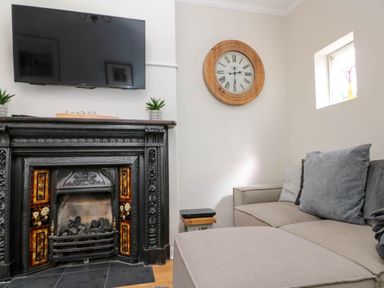 A living room with a wall mounted TV above a decorative fireplace and a sofa with cushions at Rydal Cottage in Scarborough