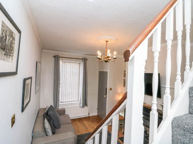 A living room with a sofa cushions pictures on the wall a window with curtains a chandelier a door and a staircase at Rydal Cottage Scarborough