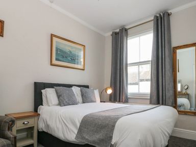 A bedroom with a bed pillows bedside table window with curtains and a mirror on the wall at Rydal Cottage in Scarborough