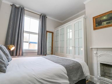 A bedroom with a bed gray curtains wardrobe and a fireplace at Rydal Cottage in Scarborough