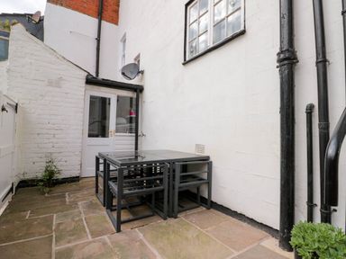 An outdoor patio area with a glass table and four chairs against white walls at Rydal Cottage in Scarborough