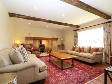 A living room with two sofas a wooden coffee table a red patterned rug exposed wooden beams a fireplace and a window with curtains at Morgans Farmhouse Bampton Oxfordshire