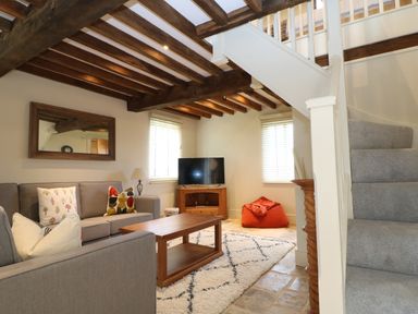A living room with grey sofas a wooden coffee table TV on a wooden stand an orange bean bag a rug and carpeted stairs at Morgans Farmhouse in Bampton Oxfordshire
