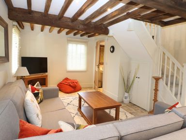 A living room with exposed wooden beams a gray sofa a wooden coffee table a television and a bean bag at Morgans Farmhouse in Bampton Oxfordshire